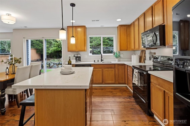 kitchen featuring visible vents, a kitchen bar, wood finished floors, black appliances, and a sink