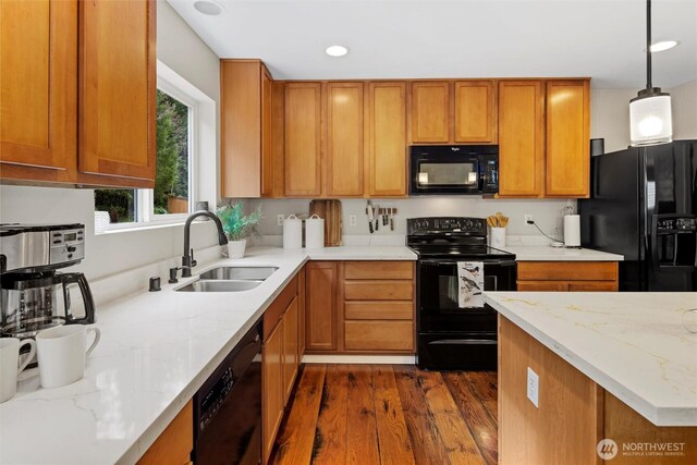 kitchen featuring dark wood-style floors, light stone countertops, a sink, black appliances, and brown cabinets