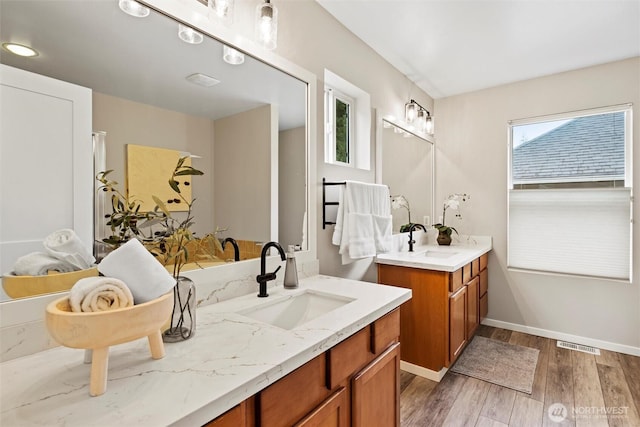 full bathroom featuring wood finished floors, baseboards, visible vents, two vanities, and a sink