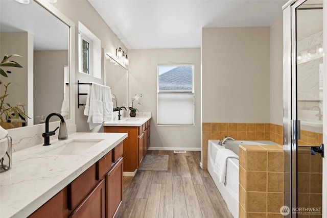 bathroom featuring two vanities, a sink, wood finished floors, a shower stall, and a bath