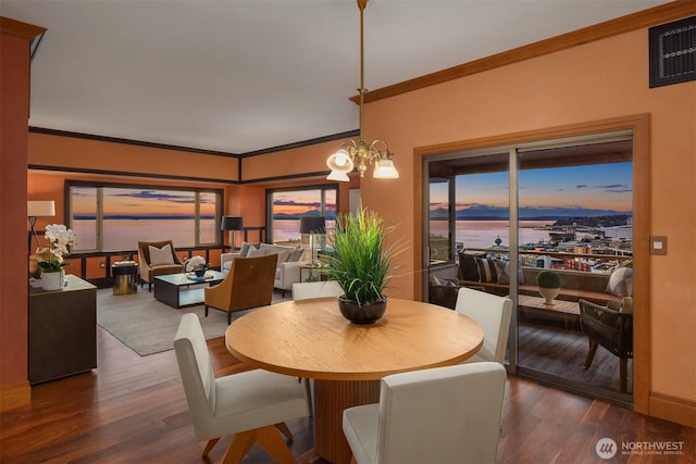 dining space featuring a water view, ornamental molding, a notable chandelier, and wood finished floors