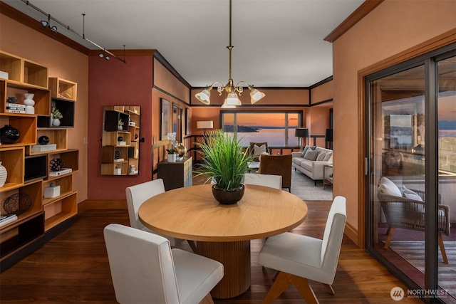 dining room with crown molding, dark wood finished floors, rail lighting, and an inviting chandelier