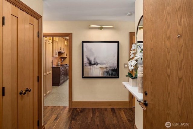 hallway featuring dark wood-type flooring, a sink, and baseboards