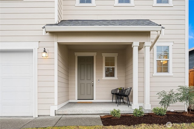 view of exterior entry with an attached garage, covered porch, and roof with shingles