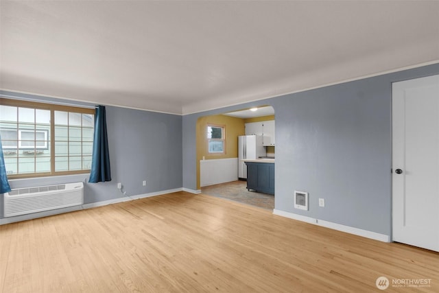 unfurnished living room featuring a wall unit AC, light wood finished floors, baseboards, and arched walkways