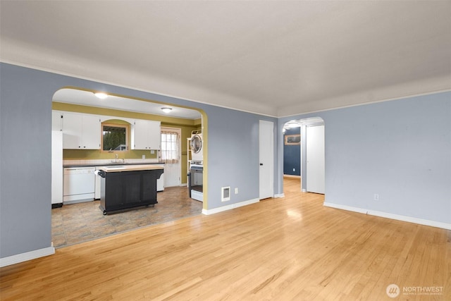 unfurnished living room featuring arched walkways, light wood-type flooring, and baseboards