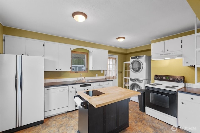 kitchen featuring white appliances, stacked washer / dryer, under cabinet range hood, white cabinetry, and a sink