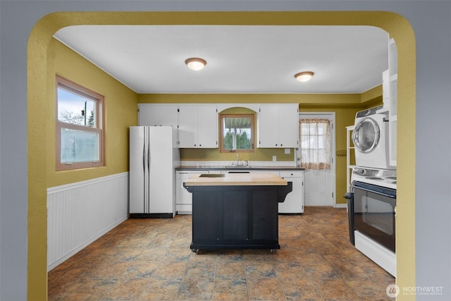 kitchen featuring a wainscoted wall, stacked washer / drying machine, stove, freestanding refrigerator, and a sink