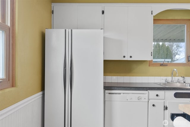 kitchen with white appliances, white cabinetry, a sink, and wainscoting