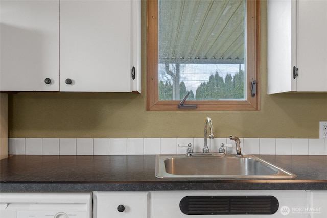 kitchen featuring dark countertops, washer / dryer, white cabinetry, and a sink