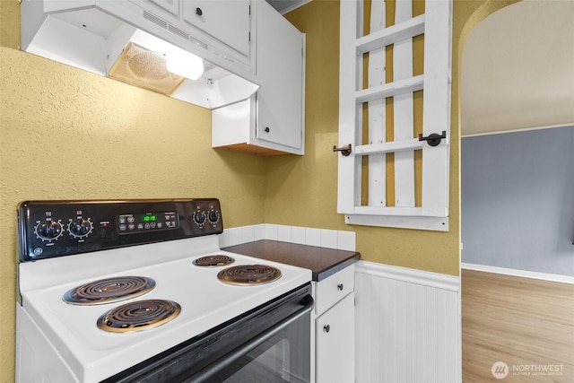 kitchen with electric range, white cabinets, wainscoting, wood finished floors, and under cabinet range hood