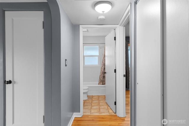 corridor with arched walkways, light wood-style flooring, and baseboards