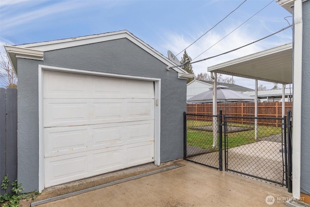 detached garage featuring driveway, fence, and a gate