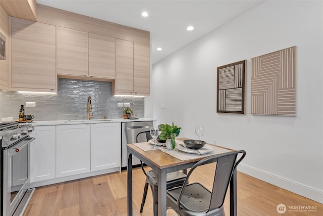 kitchen featuring decorative backsplash, appliances with stainless steel finishes, light countertops, light wood-type flooring, and a sink