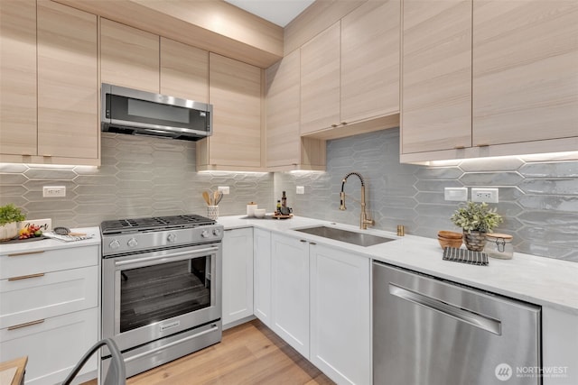 kitchen featuring stainless steel appliances, light wood-type flooring, a sink, and decorative backsplash