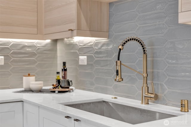 kitchen featuring white cabinets, a sink, backsplash, and light stone countertops