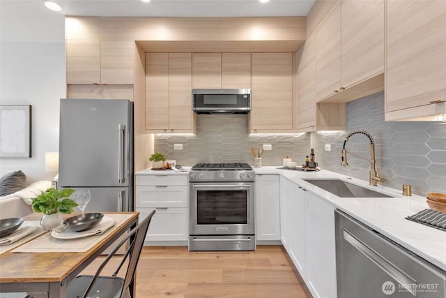 kitchen with light wood finished floors, decorative backsplash, stainless steel appliances, light countertops, and a sink