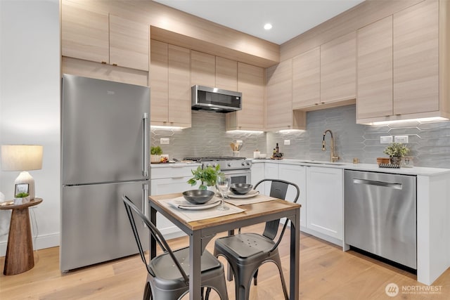 kitchen with light countertops, backsplash, appliances with stainless steel finishes, a sink, and light wood-type flooring