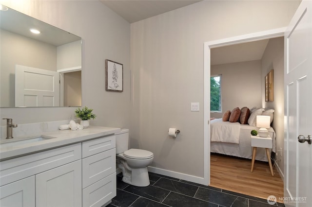 ensuite bathroom featuring baseboards, connected bathroom, toilet, tile patterned floors, and vanity