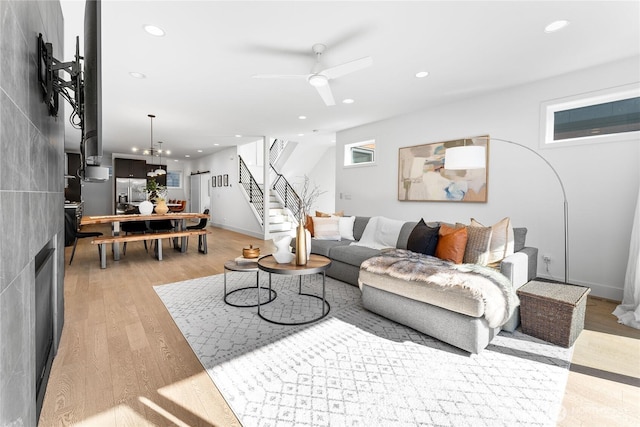 living room with light wood-type flooring, ceiling fan with notable chandelier, stairway, and recessed lighting