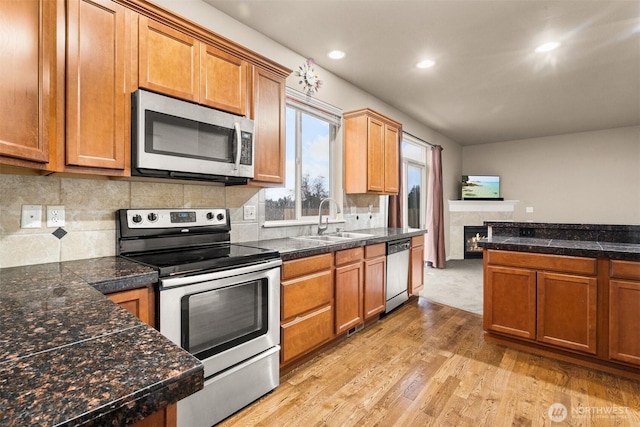 kitchen featuring tile counters, appliances with stainless steel finishes, brown cabinets, light wood-style floors, and a sink