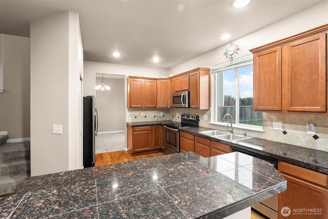 kitchen featuring brown cabinetry, tile countertops, appliances with stainless steel finishes, a sink, and backsplash