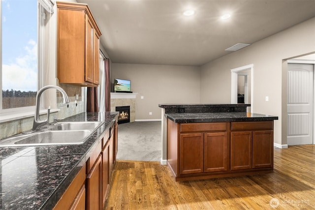 kitchen featuring dark wood-type flooring, a sink, visible vents, a lit fireplace, and brown cabinets