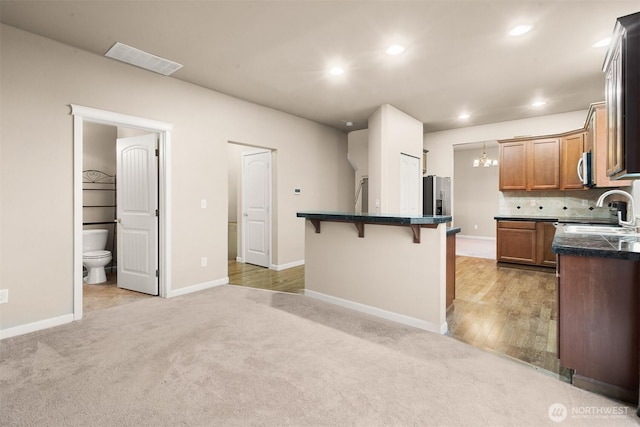 kitchen featuring tasteful backsplash, light colored carpet, visible vents, a sink, and a kitchen breakfast bar