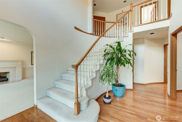 staircase featuring wood finished floors, baseboards, a high ceiling, a fireplace, and arched walkways