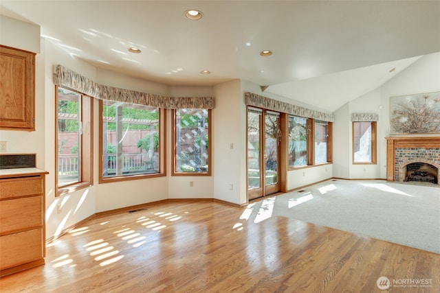 unfurnished living room featuring lofted ceiling, a brick fireplace, and light wood-style floors