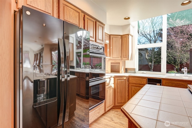 kitchen with multiple ovens, wine cooler, tile countertops, stainless steel refrigerator with ice dispenser, and a sink