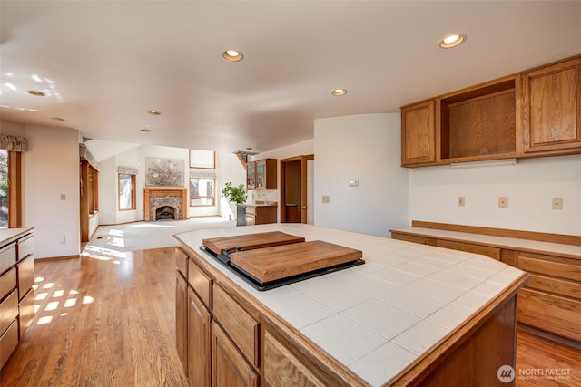 kitchen featuring recessed lighting, a fireplace with raised hearth, tile counters, and light wood finished floors