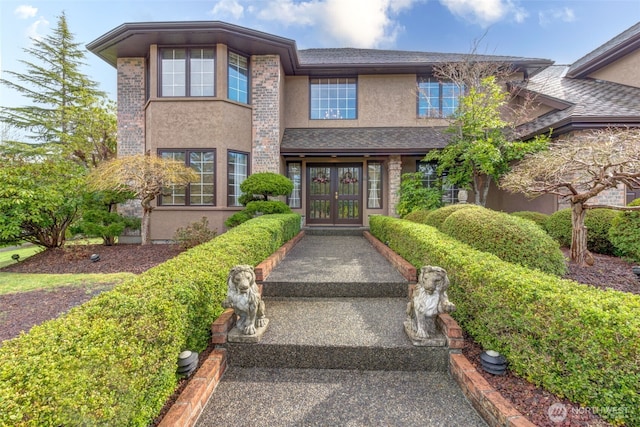 view of exterior entry featuring french doors, roof with shingles, and stucco siding