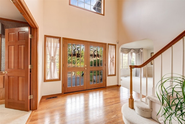 foyer featuring wood finished floors, visible vents, arched walkways, stairs, and french doors