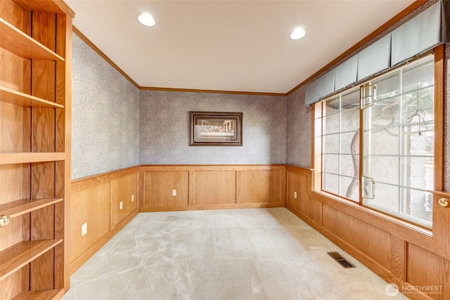 spare room featuring light carpet, visible vents, ornamental molding, and a wainscoted wall