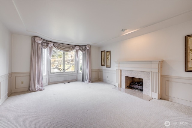 carpeted living area with a tiled fireplace, a wainscoted wall, a decorative wall, and visible vents