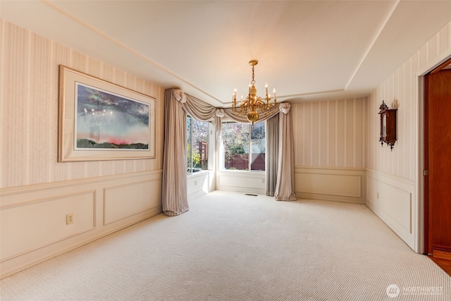 carpeted empty room featuring wallpapered walls, a decorative wall, a wainscoted wall, and a chandelier