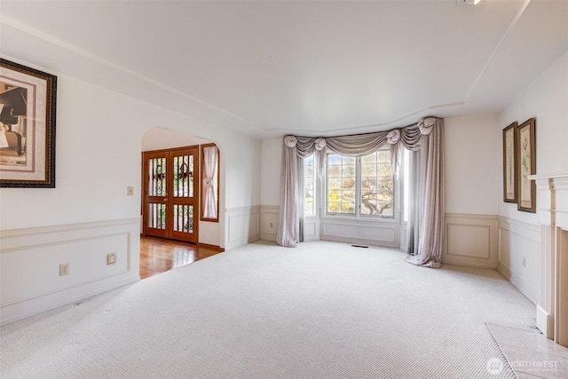 spare room featuring arched walkways, light colored carpet, a healthy amount of sunlight, and wainscoting