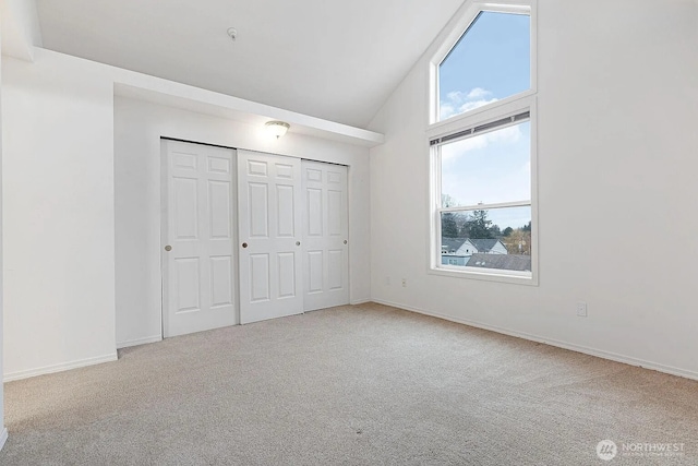 unfurnished bedroom with high vaulted ceiling, a closet, carpet flooring, and baseboards