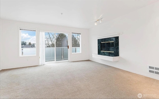 carpeted spare room with a high end fireplace, rail lighting, visible vents, and baseboards