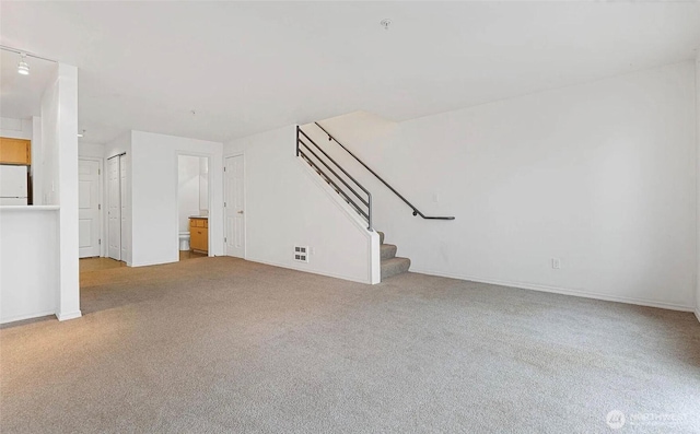 unfurnished living room with carpet floors, baseboards, and stairs