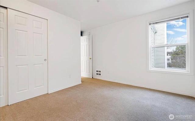 unfurnished bedroom featuring light colored carpet, a closet, visible vents, and baseboards