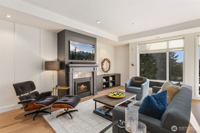 living area with recessed lighting, baseboards, a lit fireplace, and wood finished floors