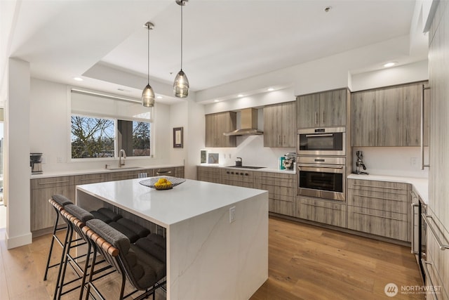 kitchen featuring wall chimney range hood, a kitchen bar, light wood-style flooring, modern cabinets, and a sink