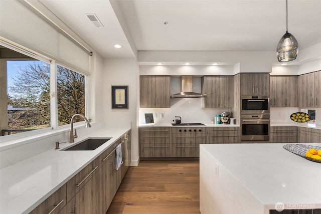 kitchen with wall chimney range hood, light countertops, stainless steel double oven, modern cabinets, and a sink