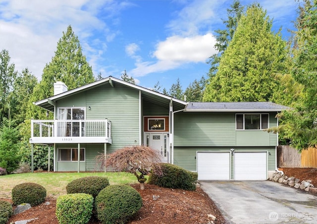 split foyer home featuring a garage, driveway, a chimney, and fence