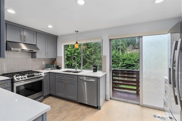 kitchen with gray cabinets, under cabinet range hood, a sink, appliances with stainless steel finishes, and light countertops