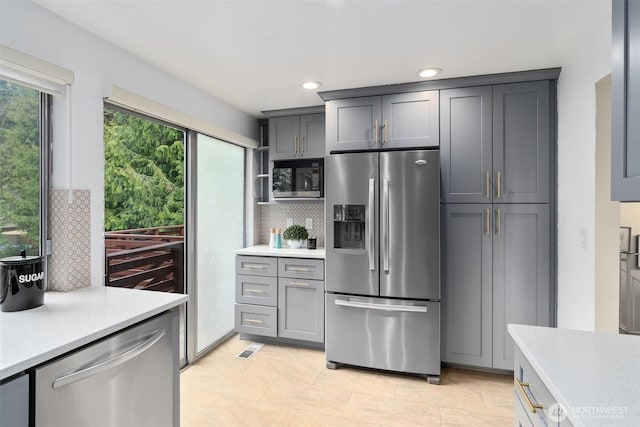 kitchen with decorative backsplash, stainless steel appliances, light countertops, and visible vents