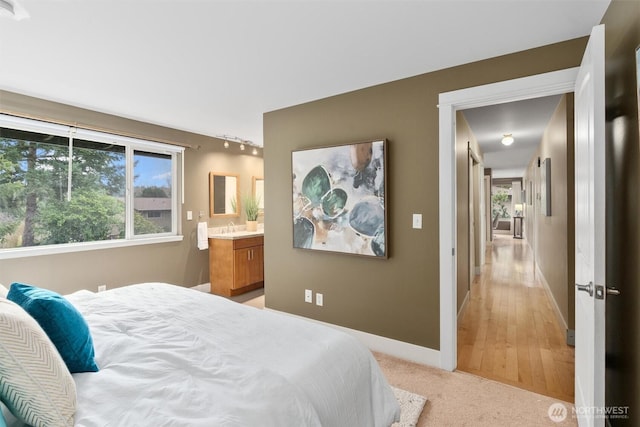 bedroom with light colored carpet, ensuite bath, and baseboards