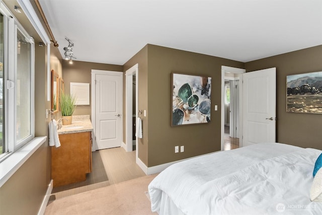 bedroom with rail lighting, multiple windows, baseboards, and a sink